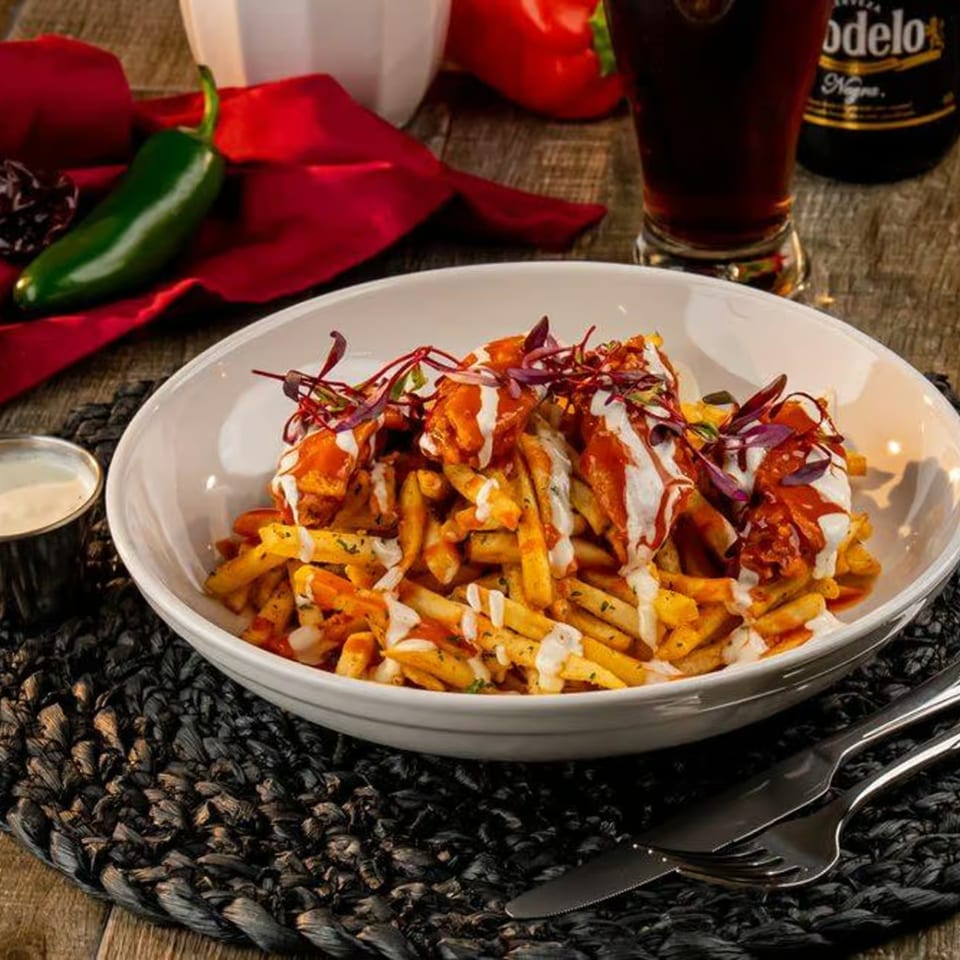 El Patio's loaded fries with chicken, sauce, and red garnish, alongside a beer and jalapeño.