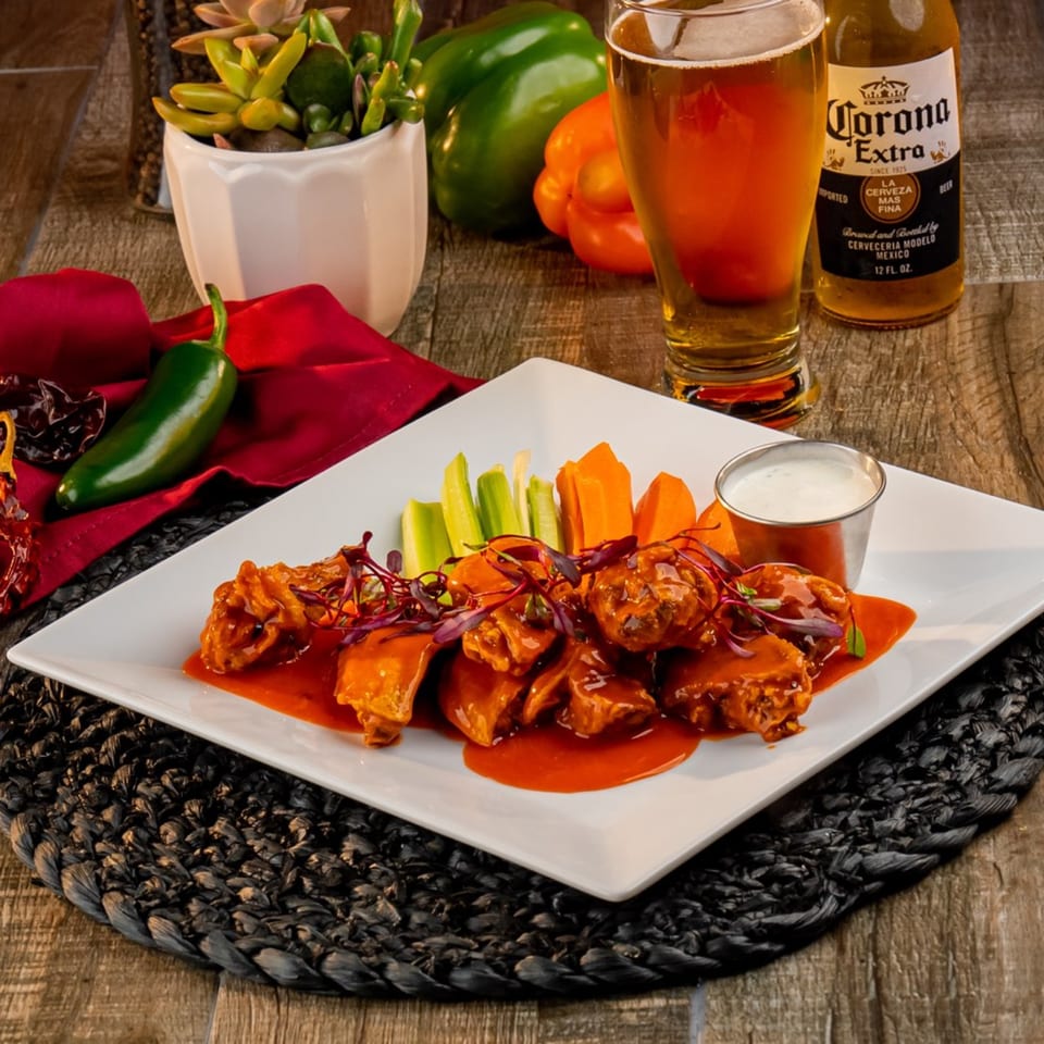 El Patio's buffalo wings with celery, carrots, ranch, and a Corona beer on a wooden table.