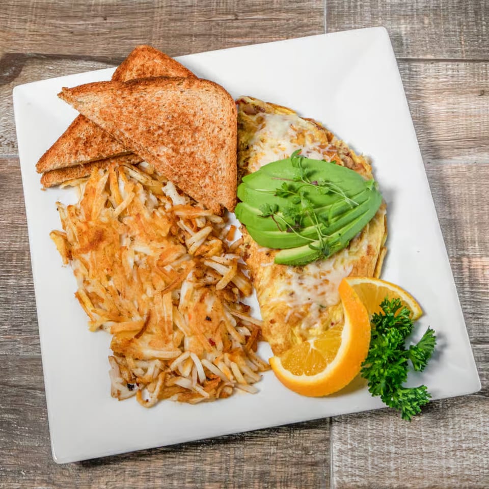 Breakfast plate with an omelet topped with avocado, hash browns, toast, and orange slices.