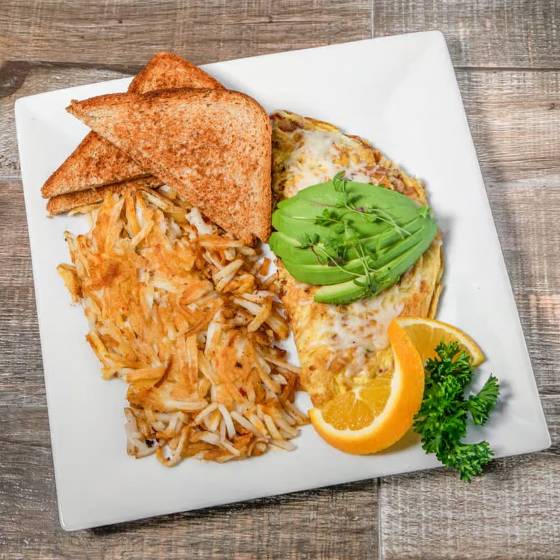 Breakfast plate with an omelet topped with avocado, hash browns, toast, and orange slices.